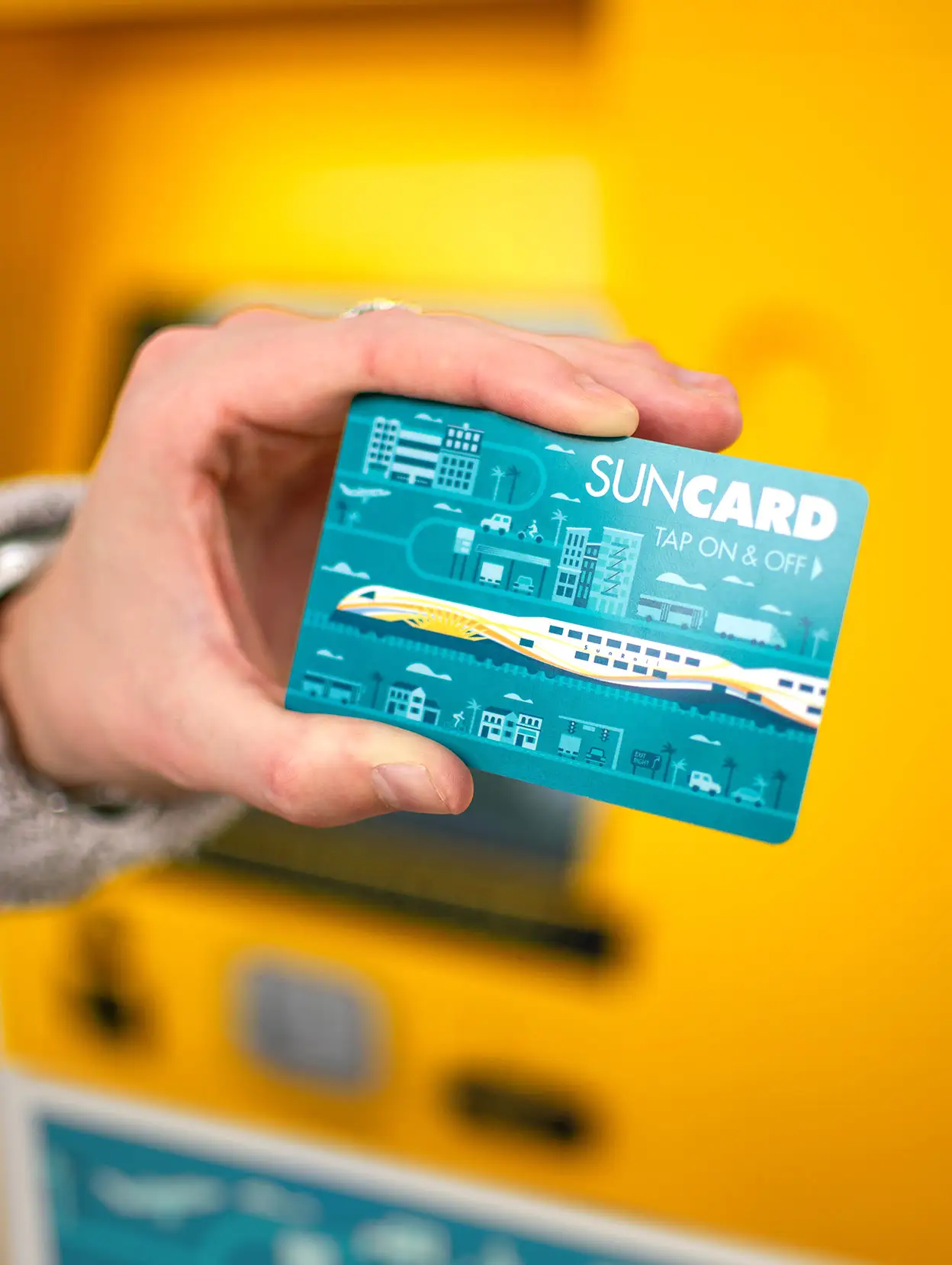 SunRail Rider holding a blue SunCard in front of a Ticket Vending Machine.