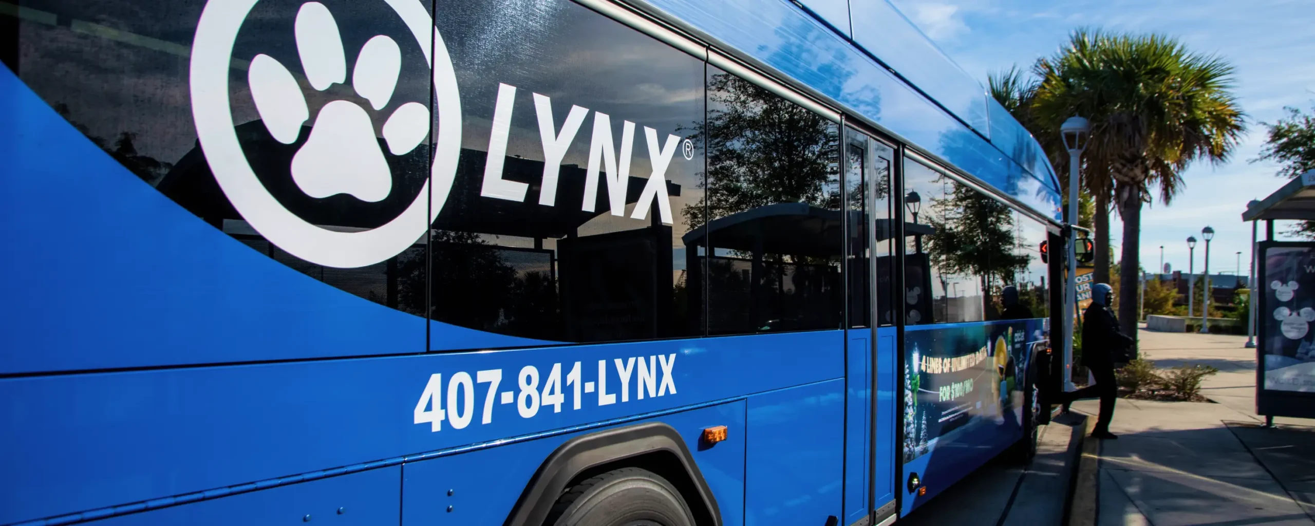 LYNX bus at the Sand Lake SunRail Station with passenger exiting bus onto curb.